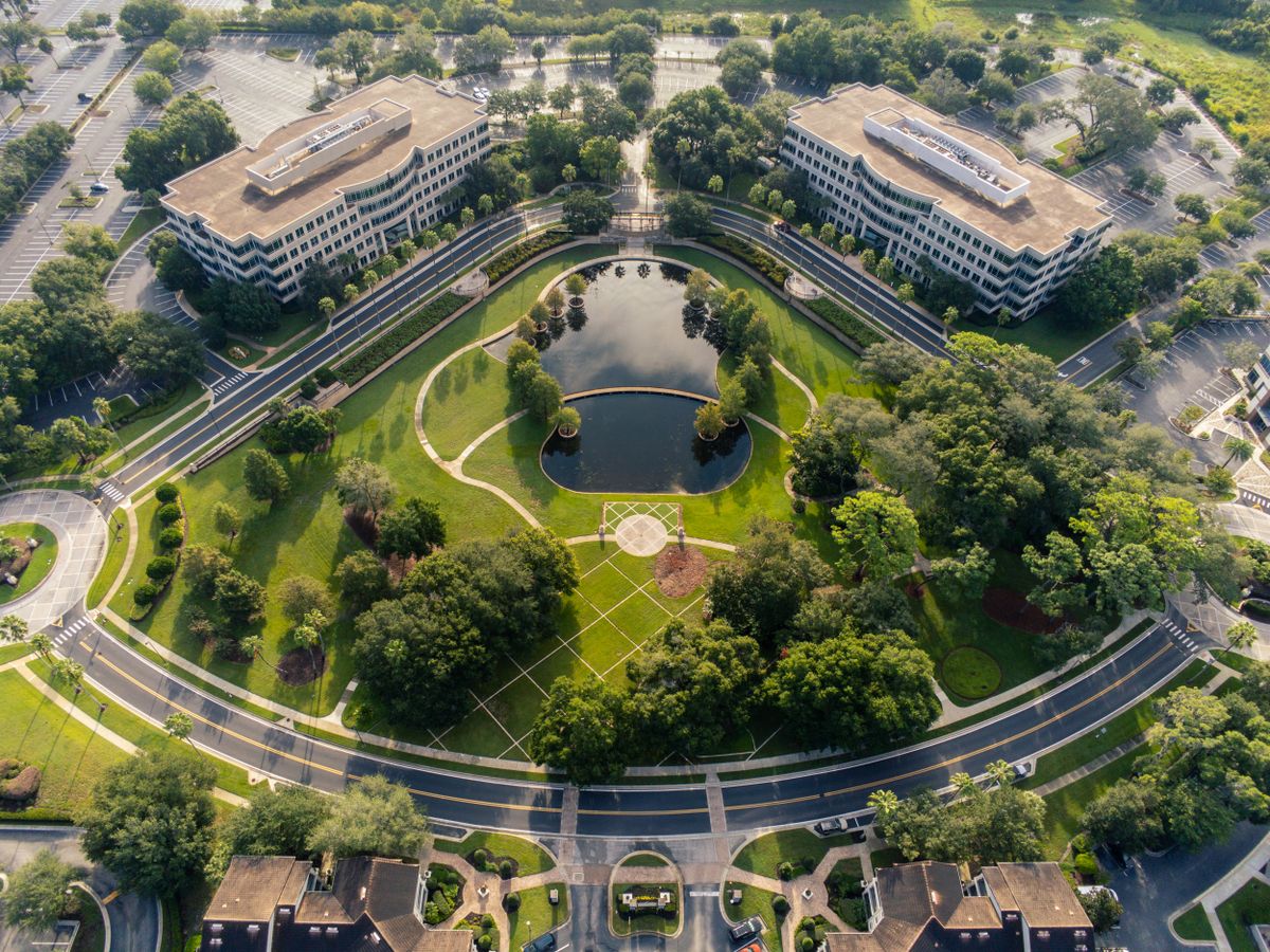 Luchtopname van een kantoorpand met omliggend terrein, water en parkeerplaatsen